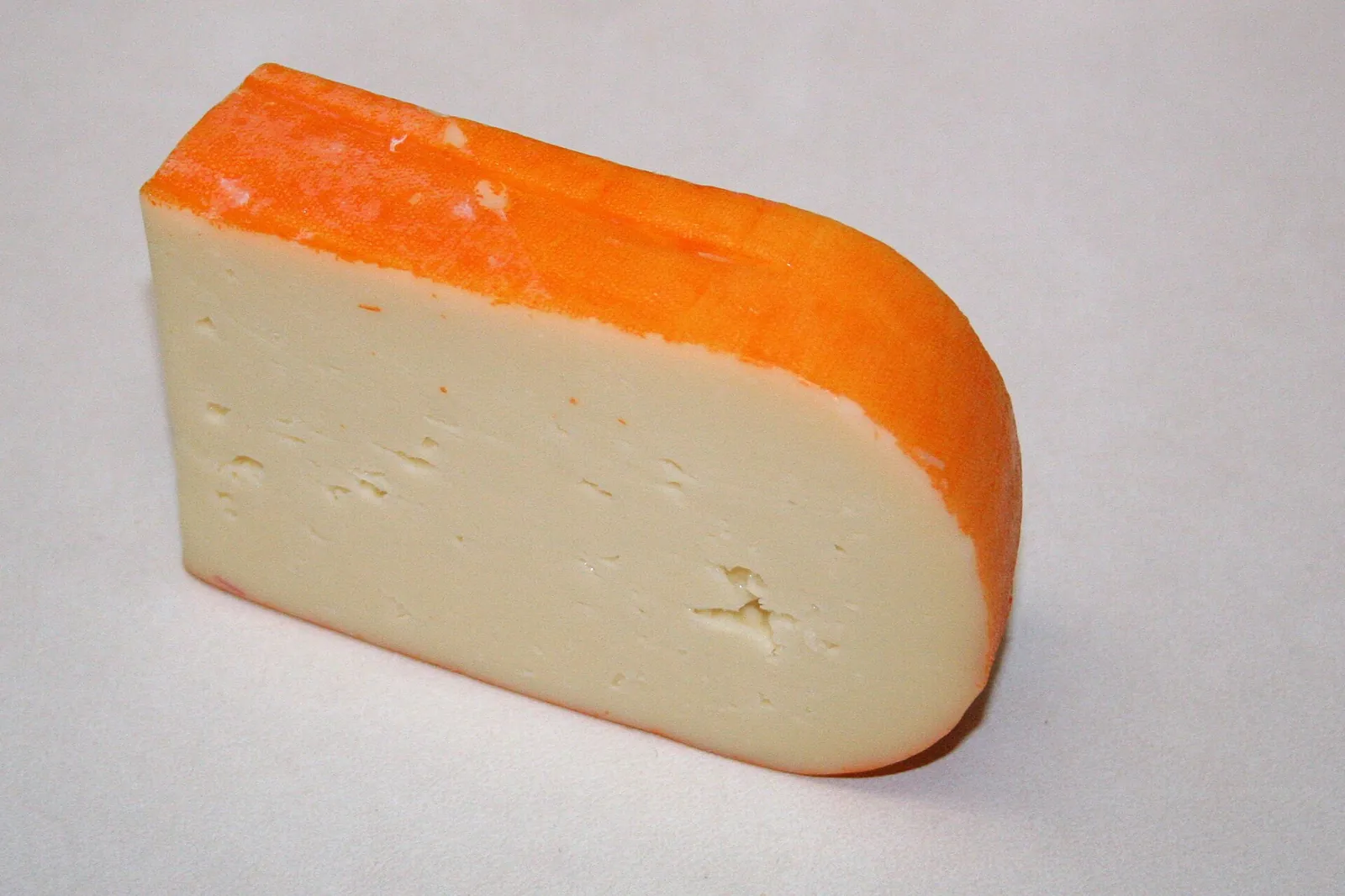 A rounded wedge of Mahon cheese with a bright orange rind and smooth pale interior