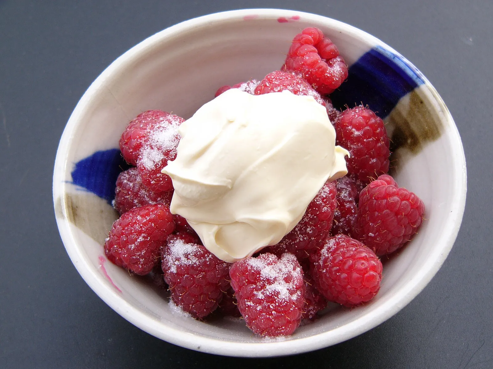 White bowl of fresh raspberries dusted with sugar and topped with a spoonful of thick creme fraiche.