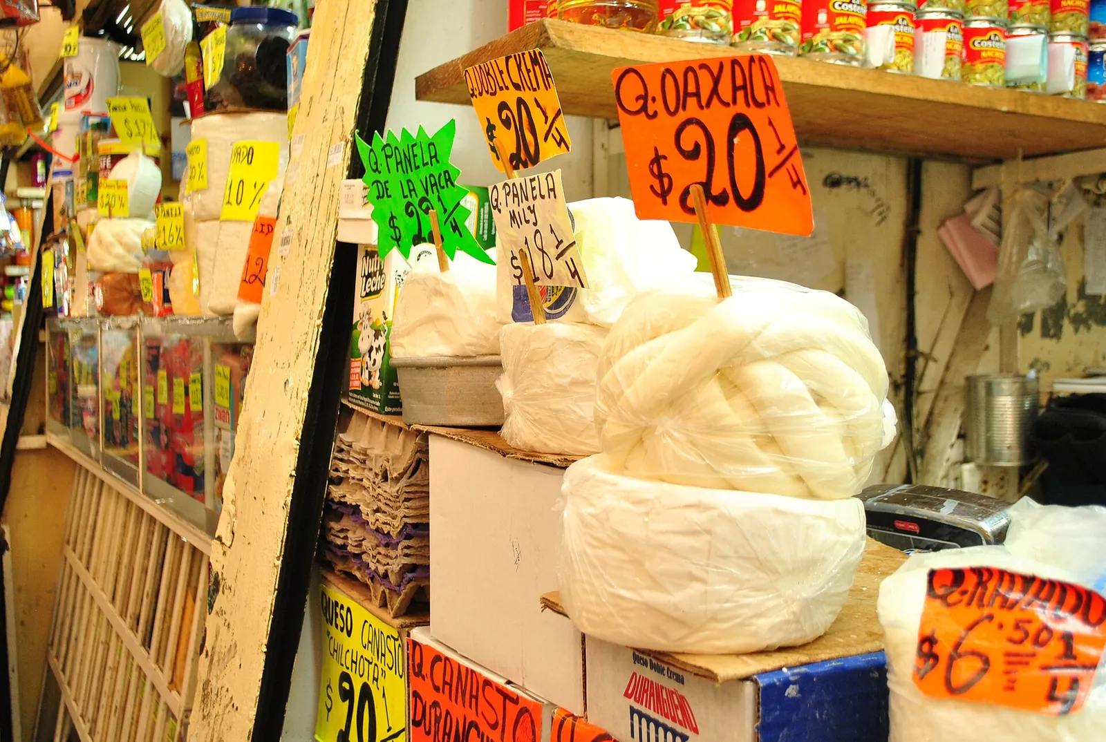 A market stall in Xochimilco, Mexico City, with balls of white Oaxaca cheese and rounds of fresh cheese under bright handwritten price signs.