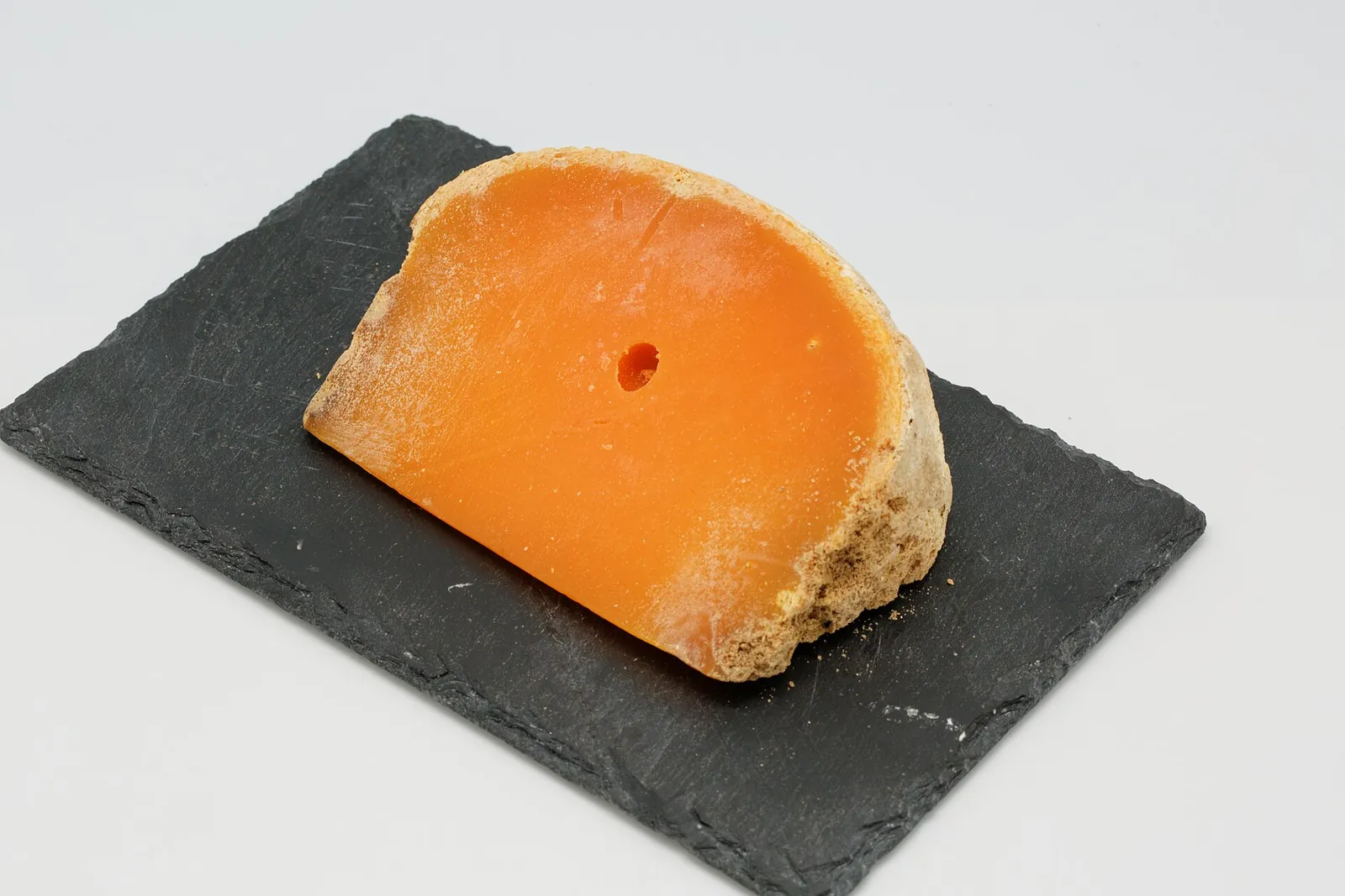 A wedge of extra-aged Mimolette with a bright orange paste and pitted rind on slate