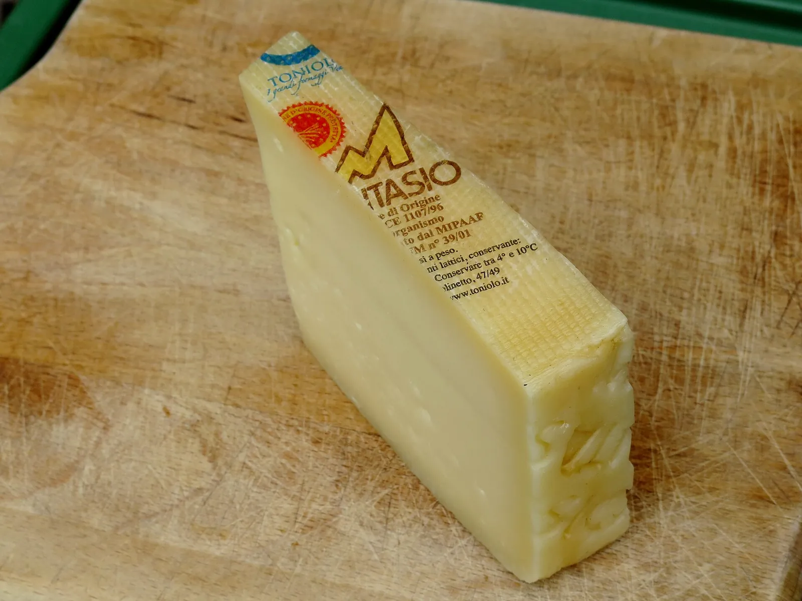 A wedge of Montasio with its rind and DOP label on a wooden board