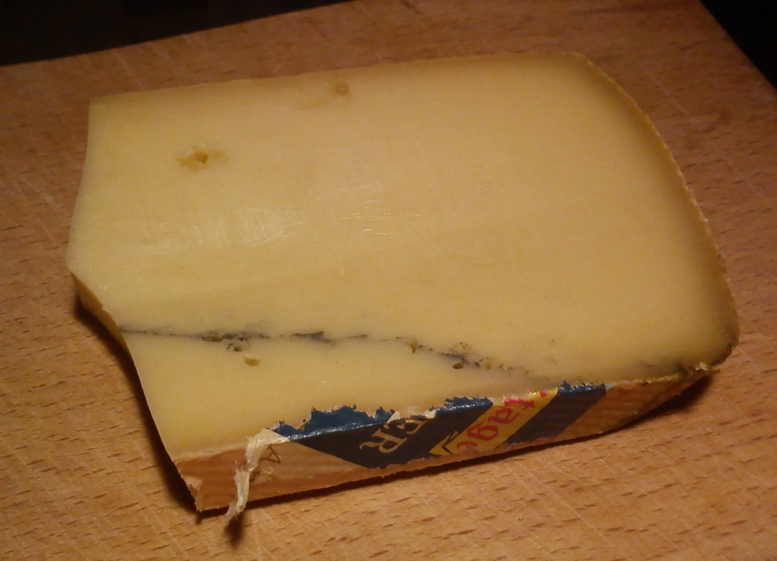 A wedge of Morbier with the dark ash line through the middle of pale yellow paste, on a wooden board