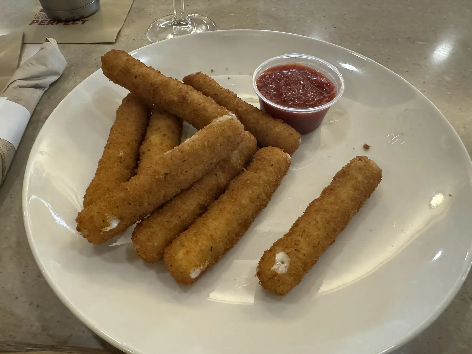 Breaded mozzarella sticks on a white plate with a cup of marinara