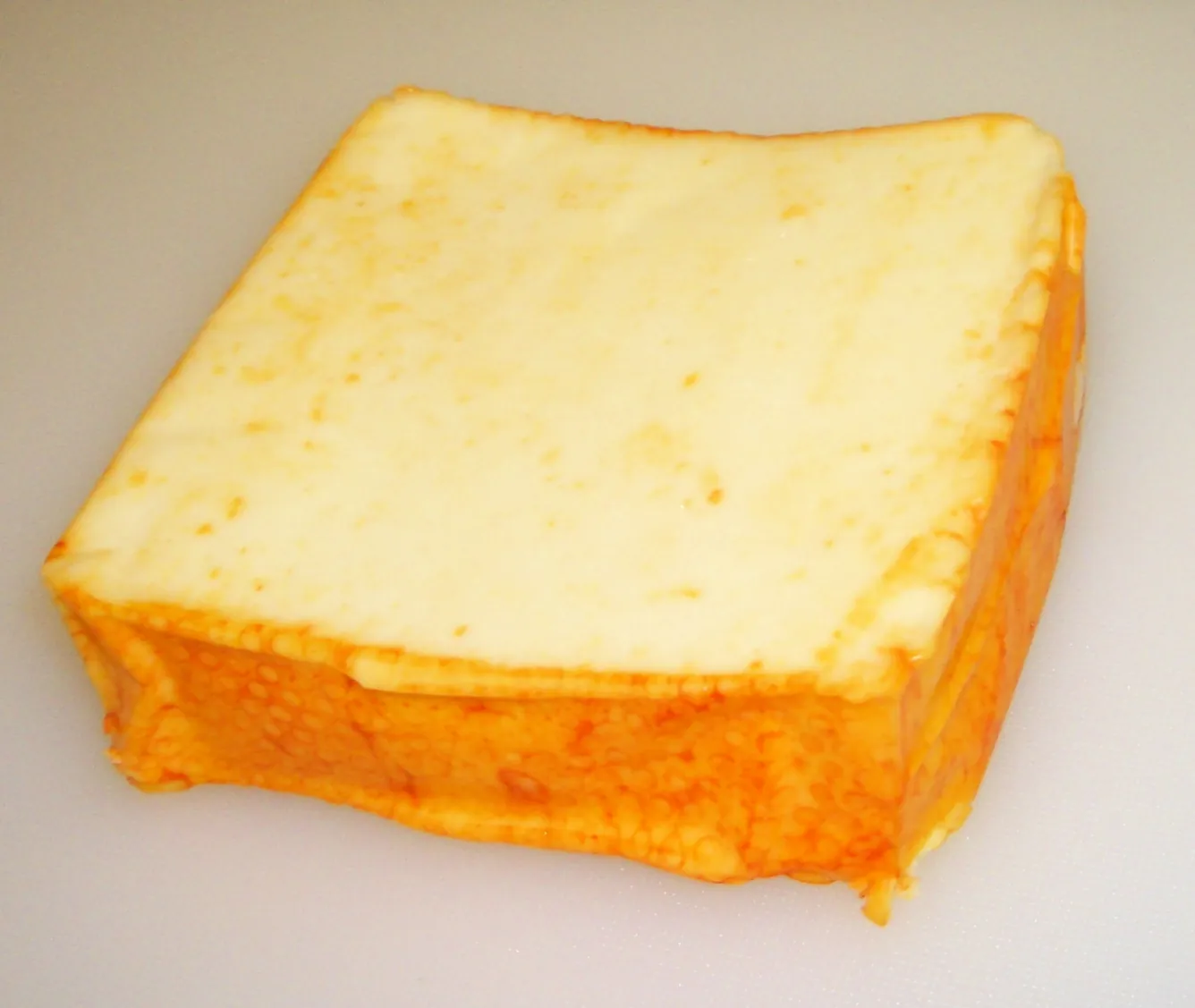 A block of Muenster cheese with its orange rind
