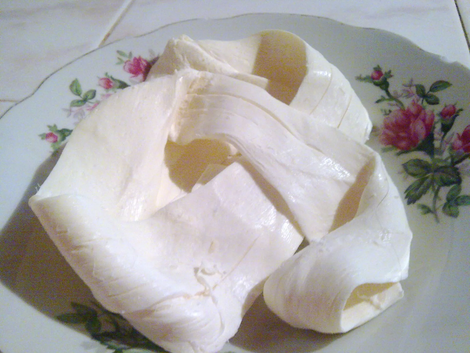 Oaxaca cheese partly unwound into soft white strands on a floral plate