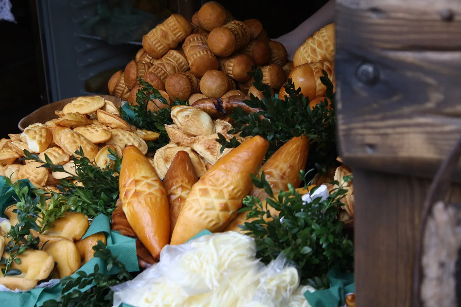 A heap of carved smoked oscypek sheep cheeses with white strands and green sprigs on a market table