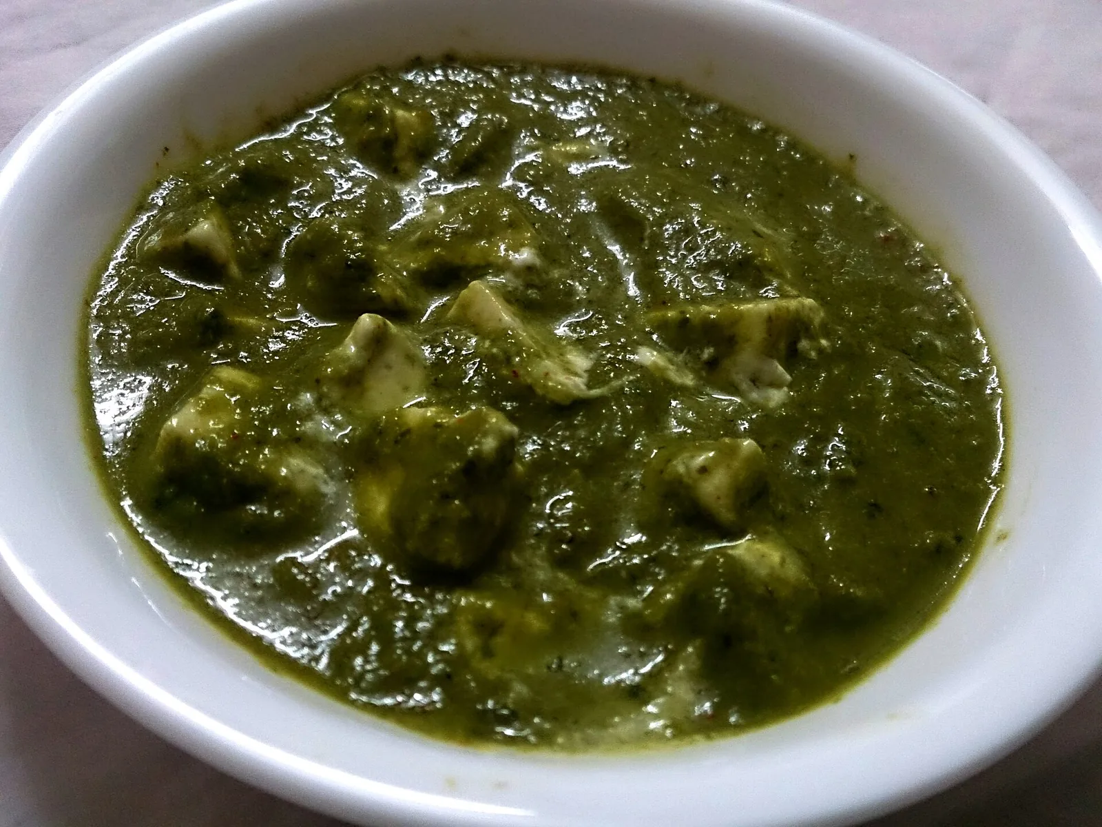 A bowl of palak paneer: cubes of paneer in a green spinach gravy