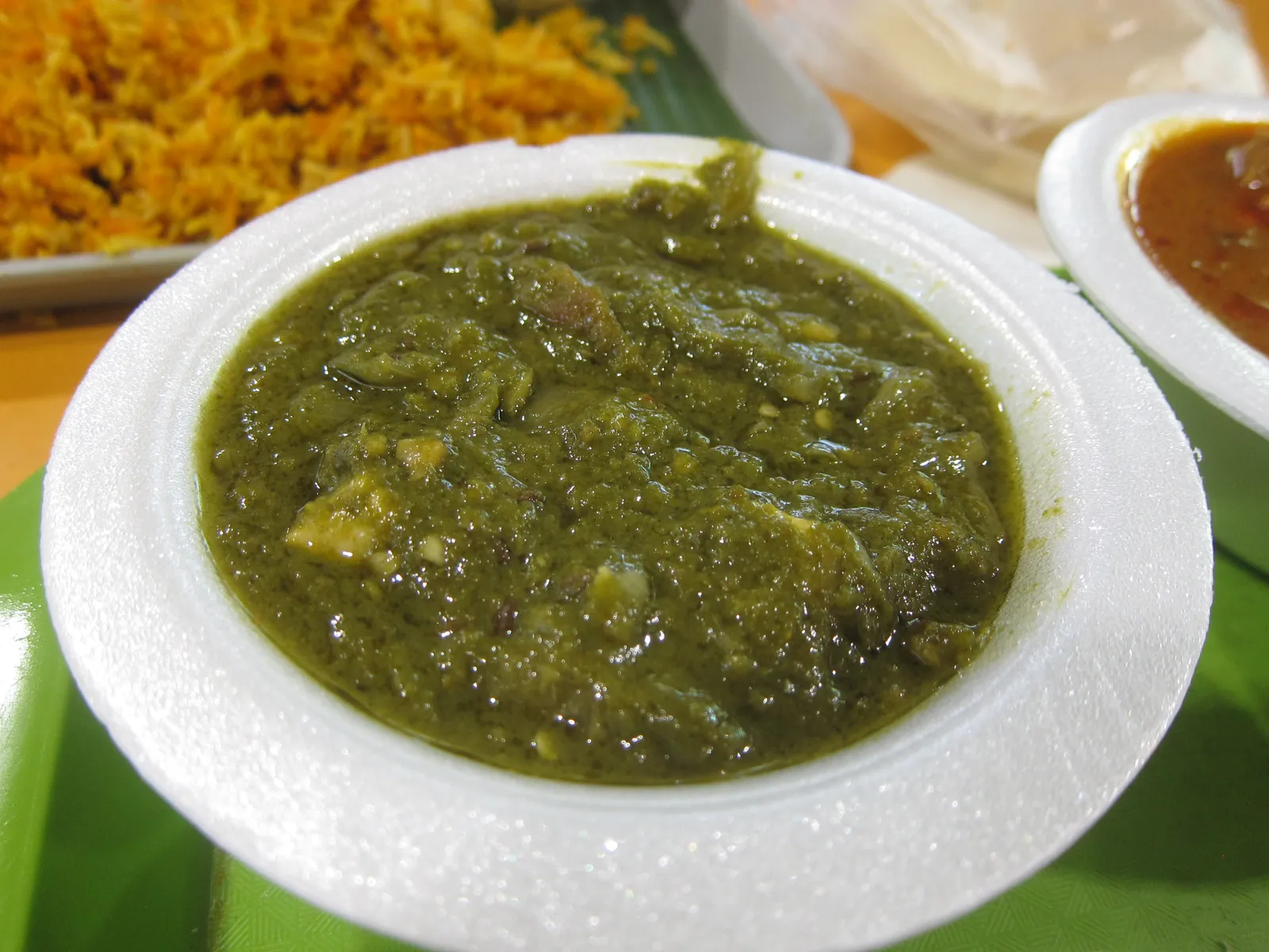 A white bowl of palak paneer, a thick green spinach gravy with soft paneer cubes, served with rice and sides