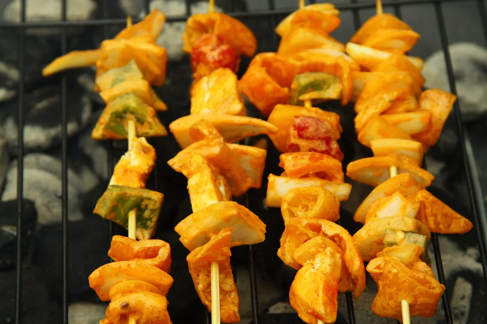Skewers of marinated paneer cubes with peppers and onion, charred orange-red from the grill, lined up over hot coals