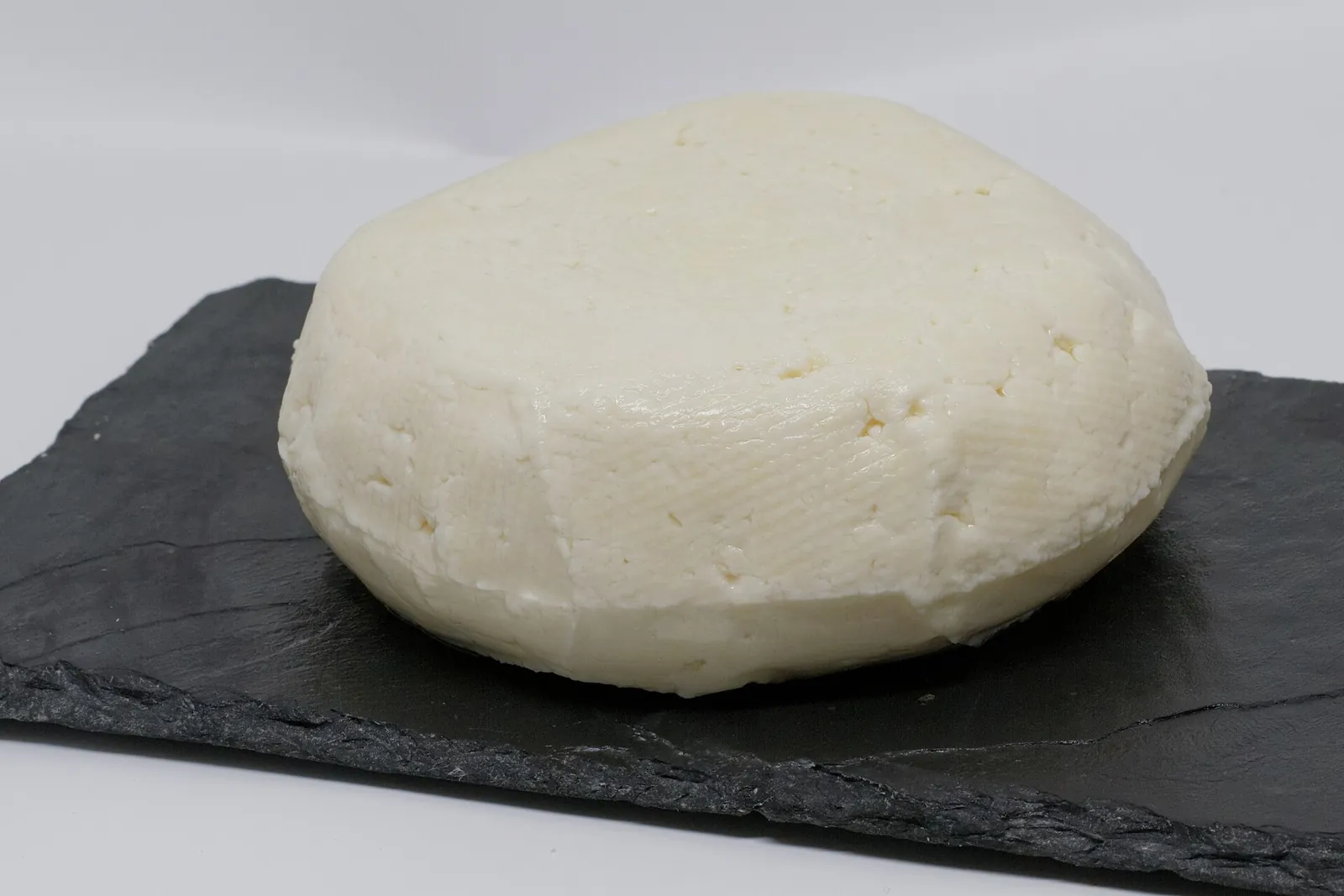 A round white Panela cheese with a basket weave texture on a slate board