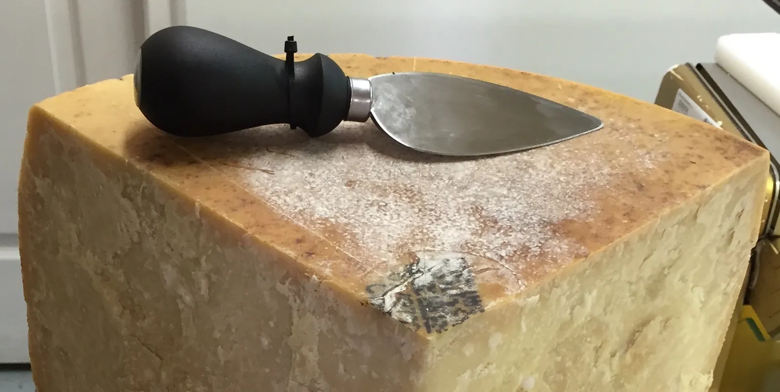 A large block of Parmesan with a short Parmesan knife resting on top