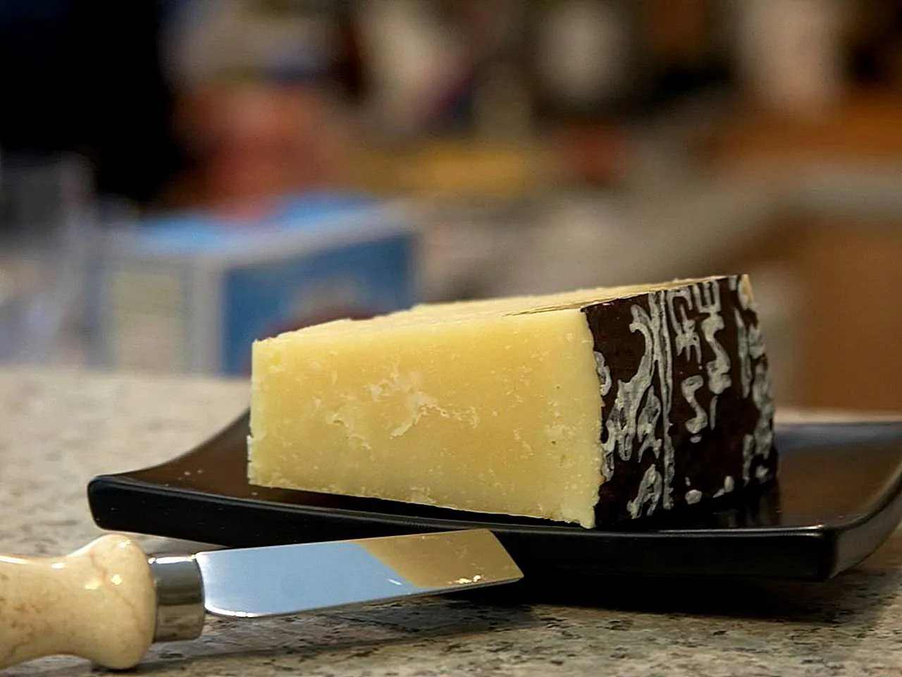 A wedge of Pecorino Romano with its dark rind on a slate board beside a cheese knife