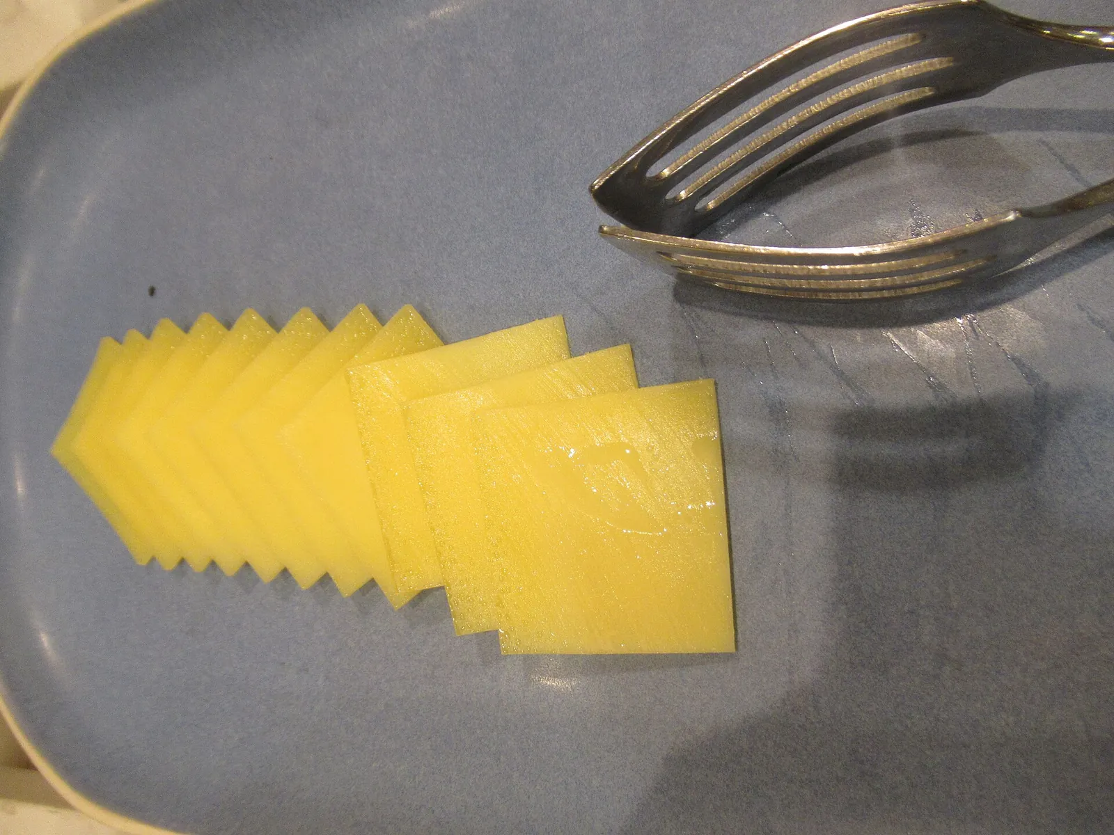 Neat slices of yellow cheese fanned out on a gray plate beside a fork, showing a single serving.