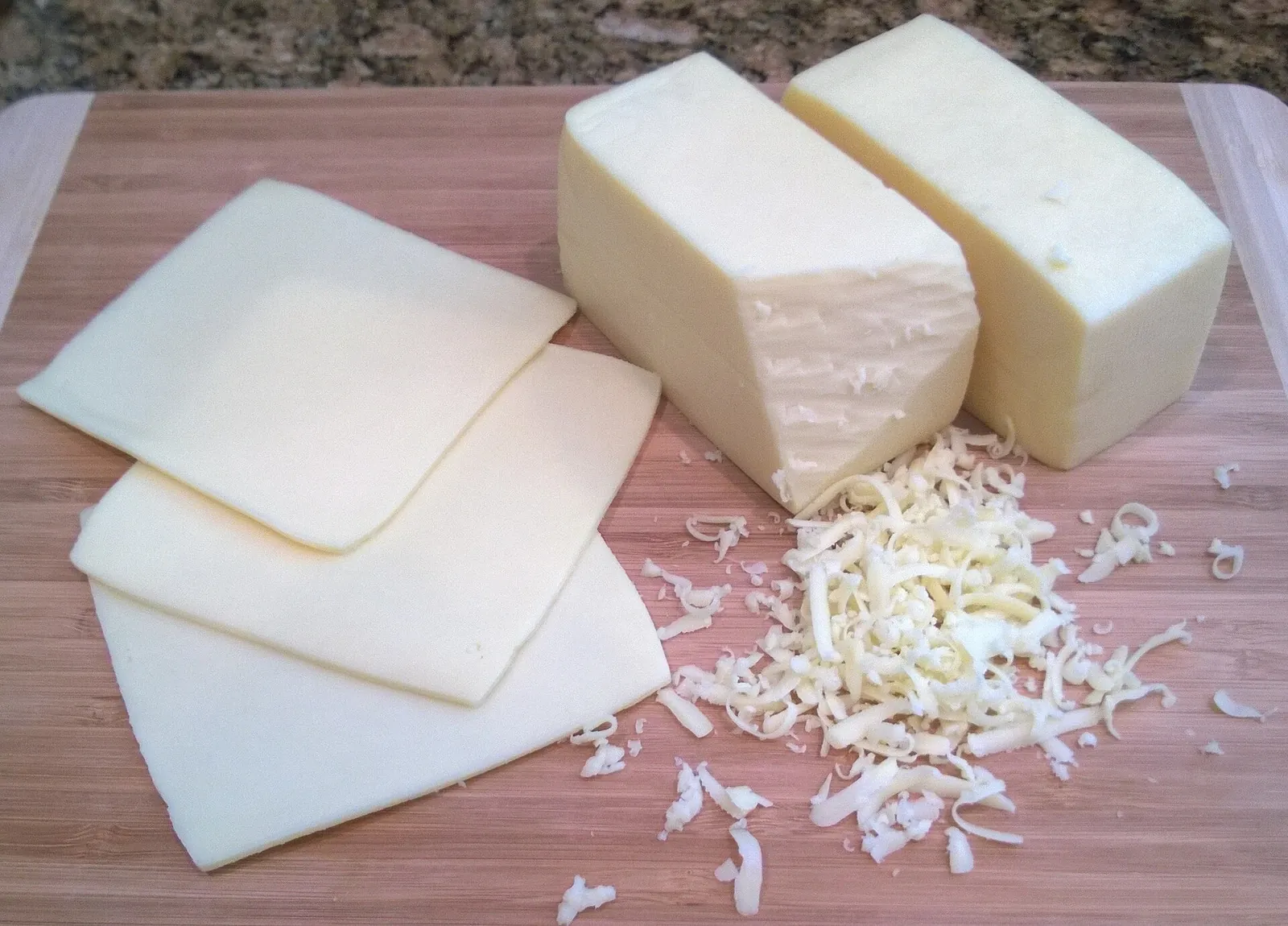 Pale yellow blocks and slices of Butterkase with grated cheese scattered on a wooden board, showing its smooth, even paste