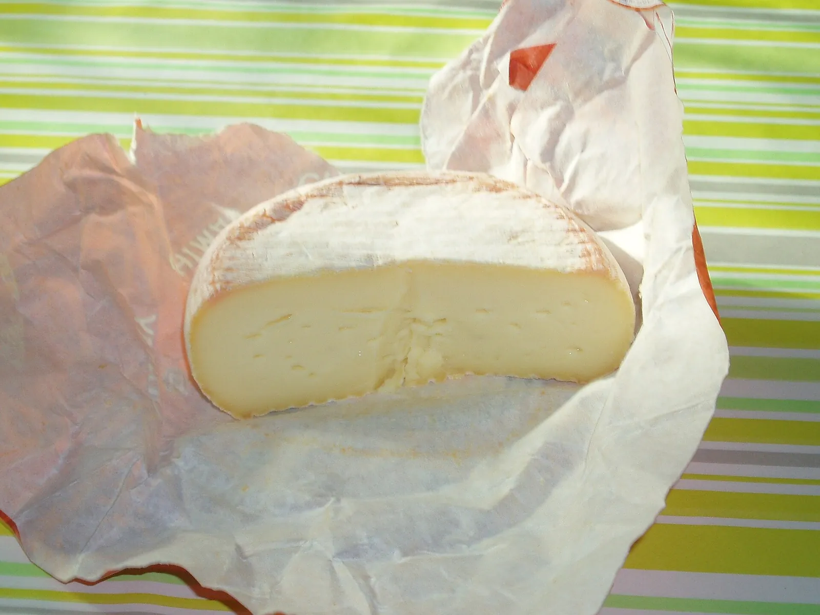 A halved round of Chimay cheese on paper wrapping, showing its soft pale paste and thin washed orange rind
