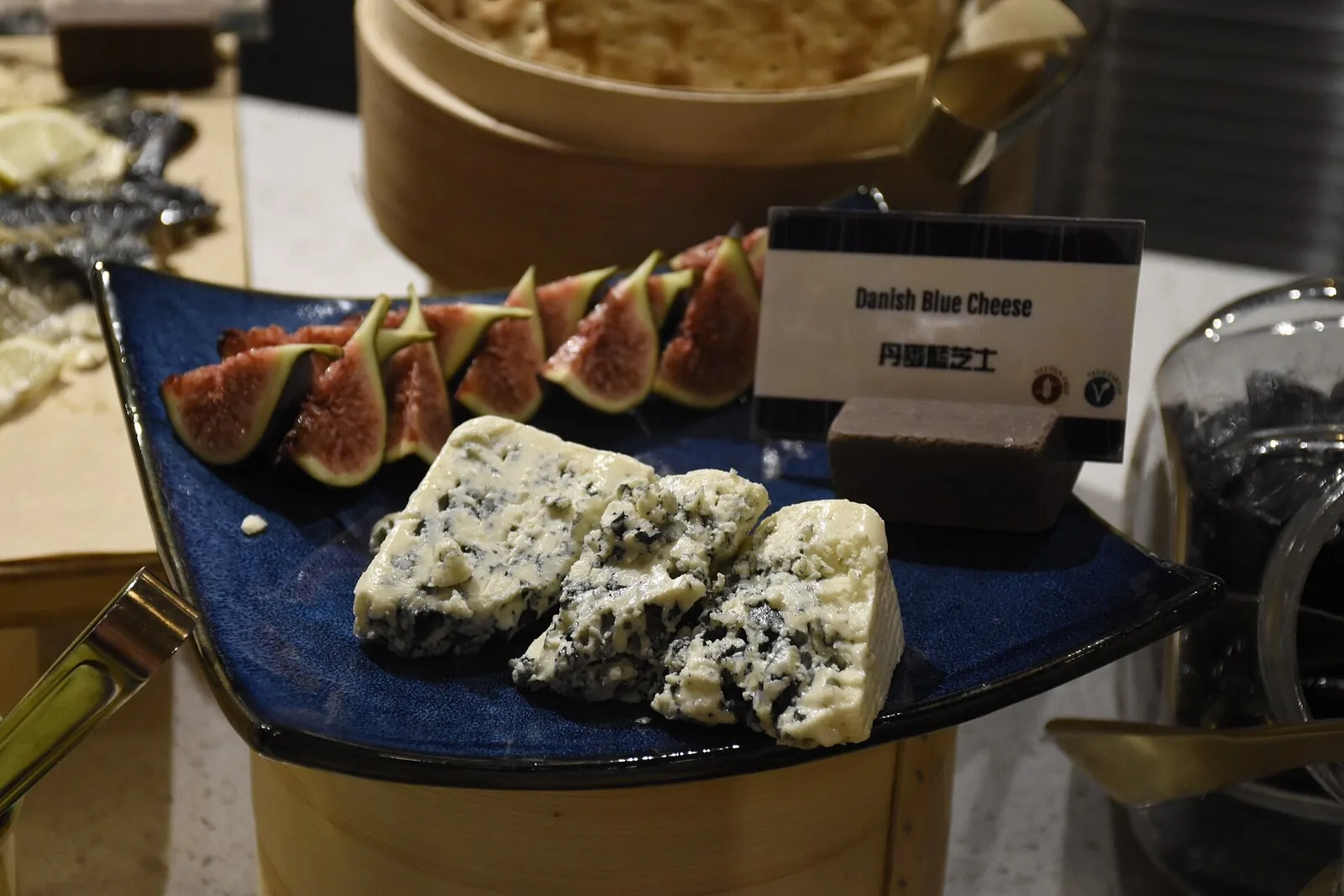 Crumbled pieces of Danish Blue with dense blue green veining, served on a dark blue dish with fresh fig slices