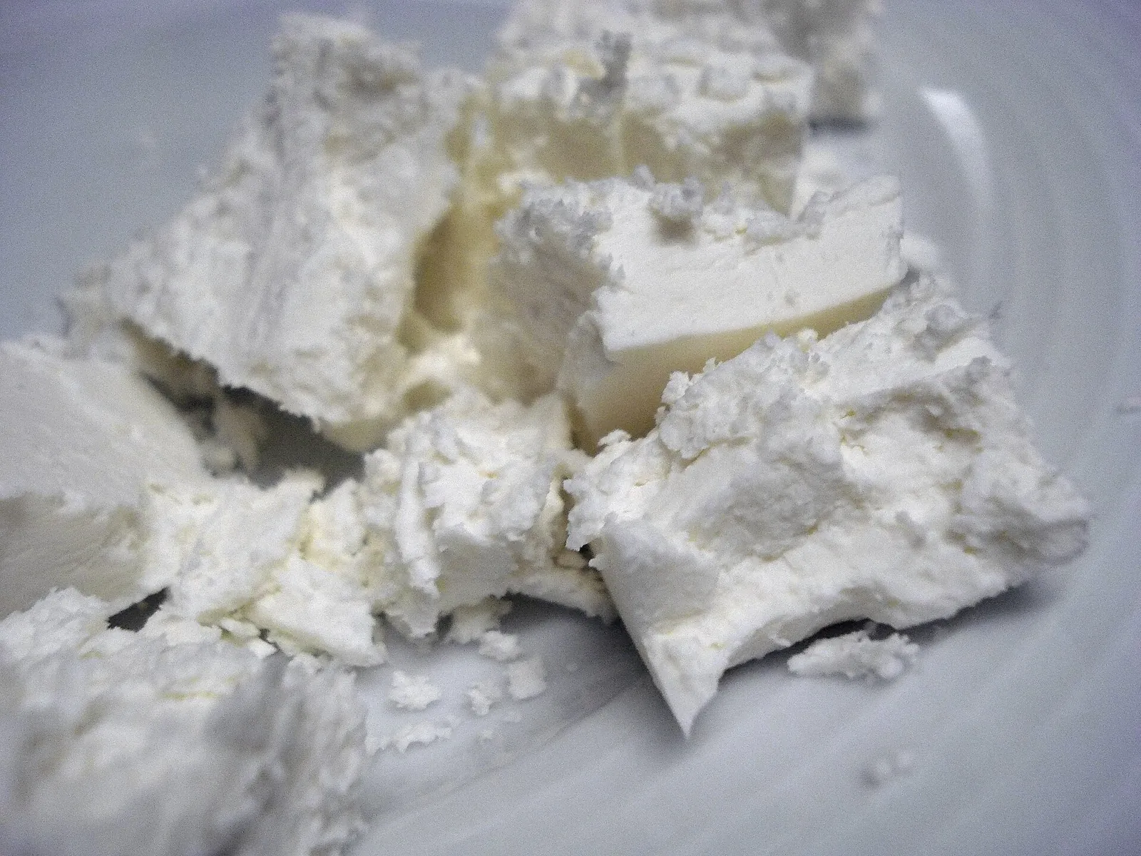 Soft, crumbled pieces of white Manouri cheese on a plate, showing its fine, creamy and slightly moist texture