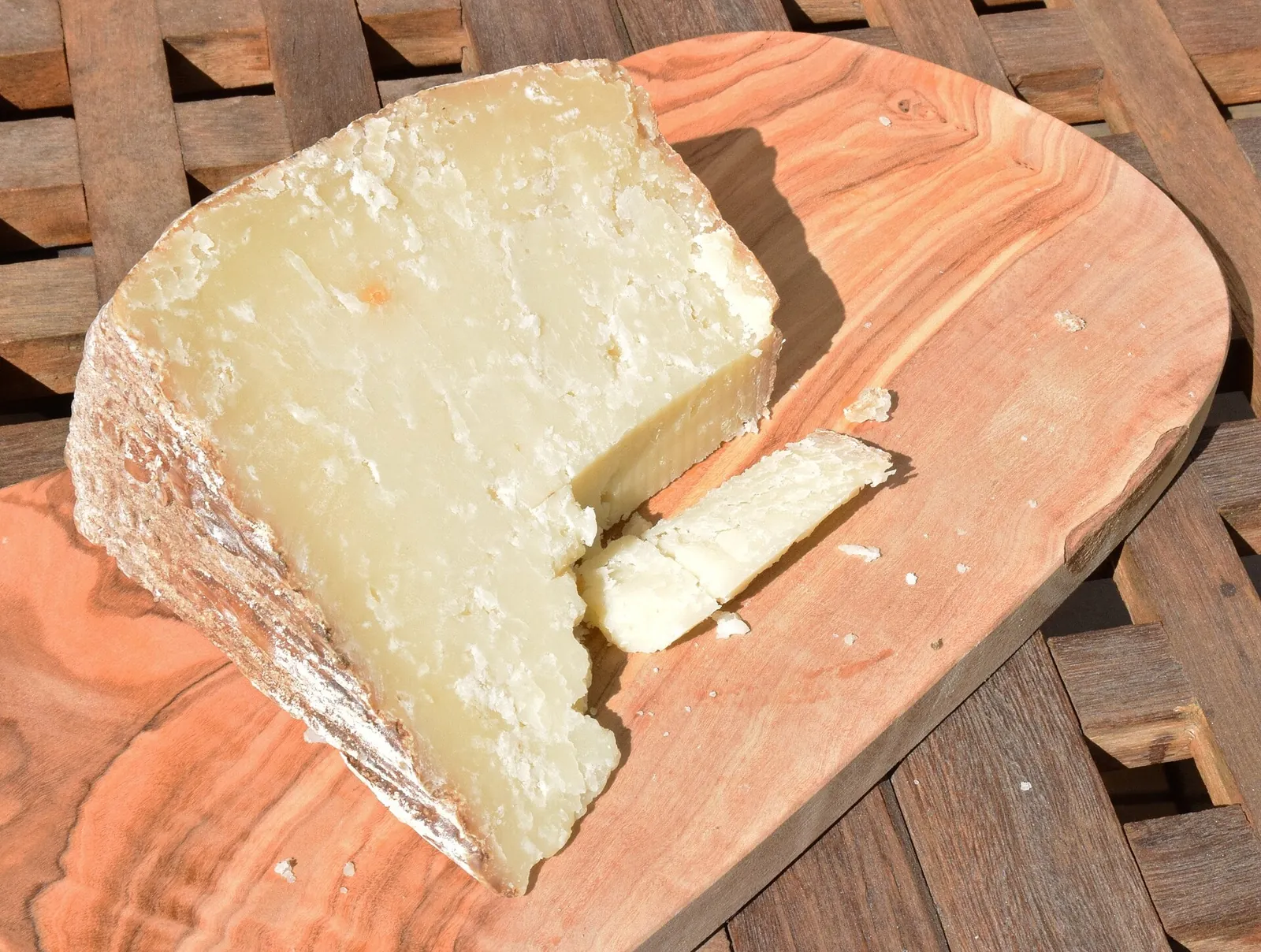 A large wedge of Pecorino Sardo with a pale, firm paste and a rough natural rind, with a small slice cut beside it