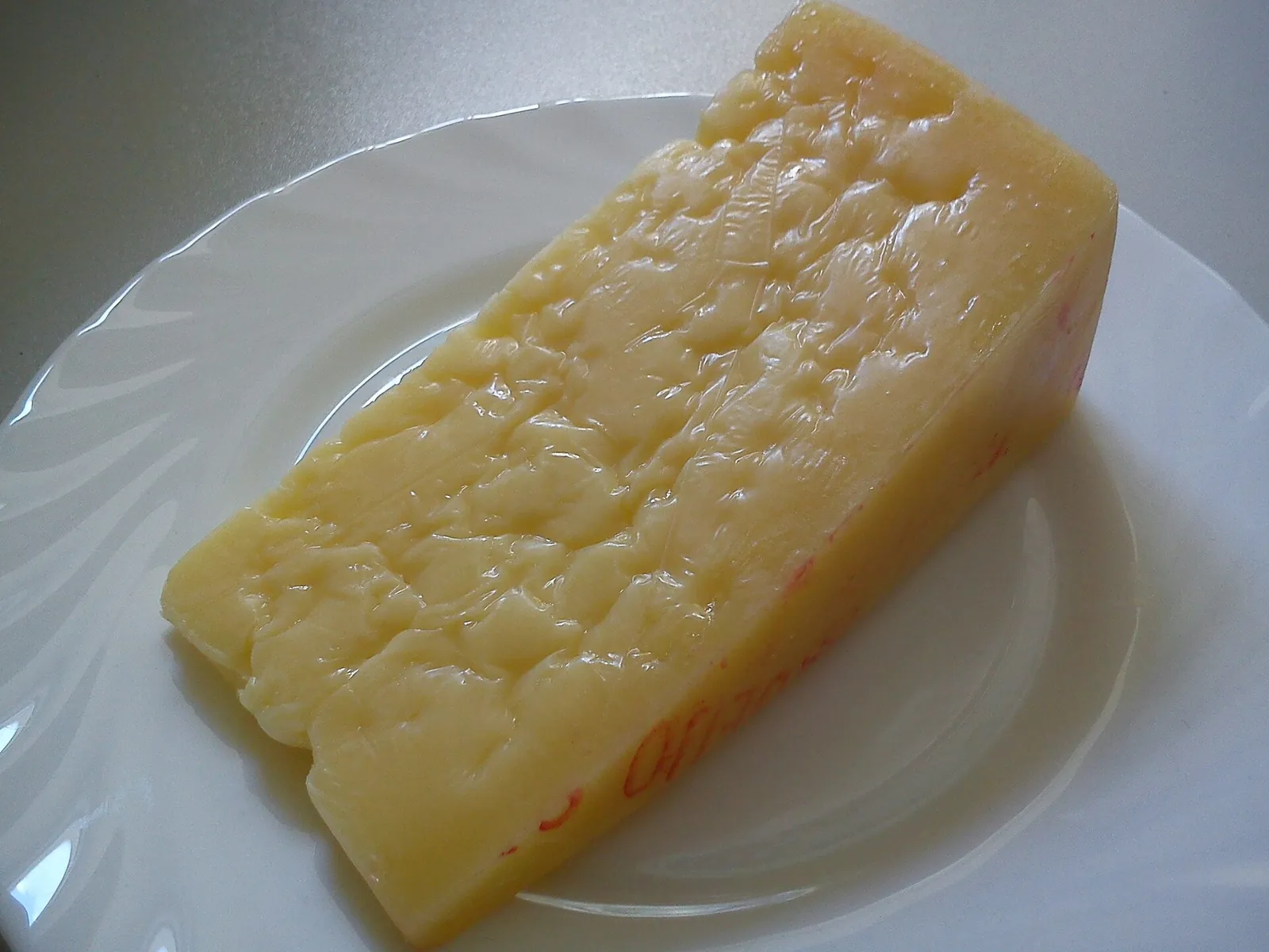 A wedge of Sao Jorge cheese on a white plate, showing a firm, pale yellow paste with small eyes and a thin rind