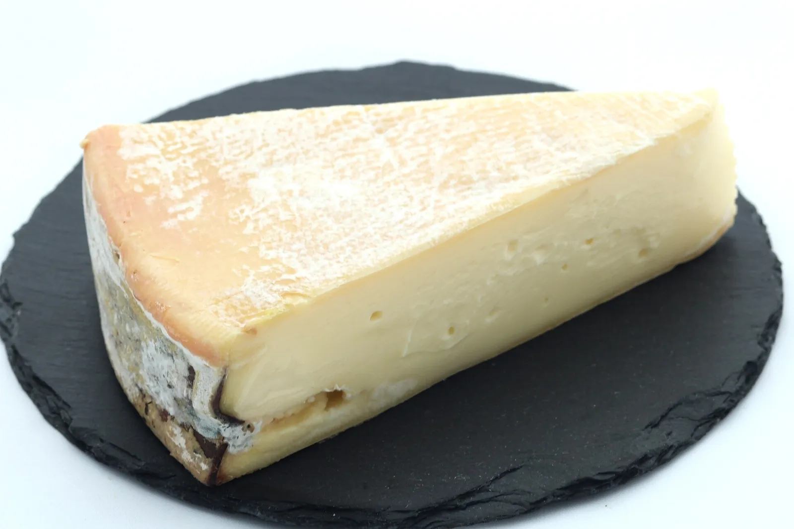 A wedge of Vacherin Mont d'Or on a black slate board, showing its bloomy orange rind and soft cream colored paste