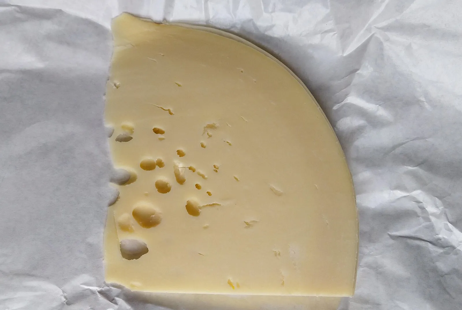 A thick slice of provolone piccante with small holes, on white paper