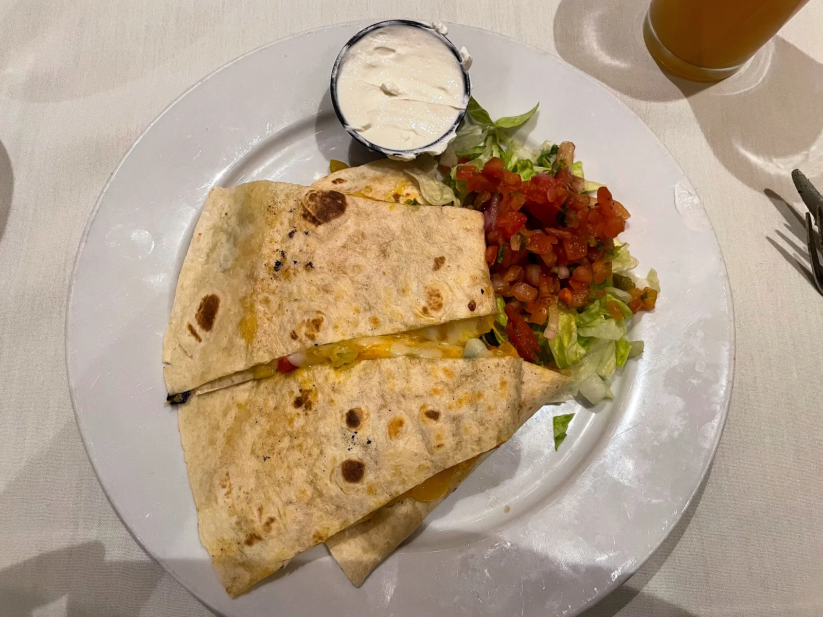 A folded flour tortilla quesadilla cut into wedges on a white plate with sour cream, salsa and lettuce
