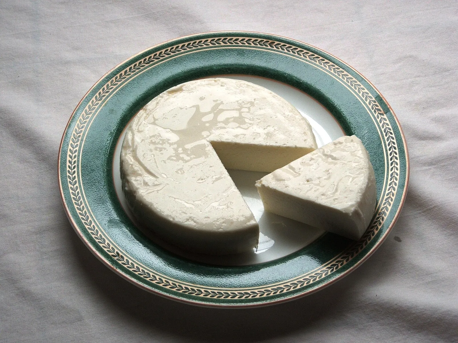 A round of white queso fresco with a wedge cut out, on a plate