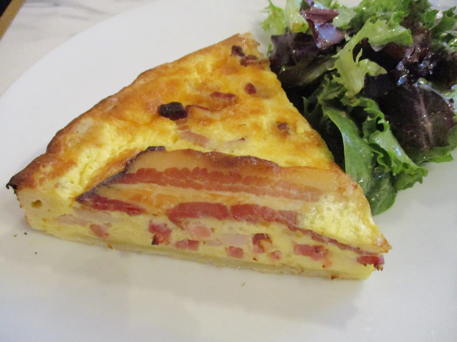 A wedge of quiche Lorraine with a golden custard filling and strips of bacon, served with a small green salad