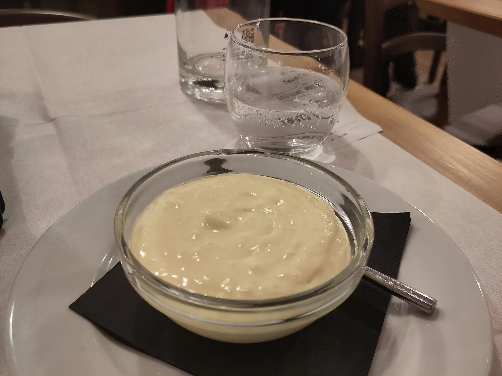 A glass bowl of thick, pale mascarpone cream on a restaurant table beside a water glass.