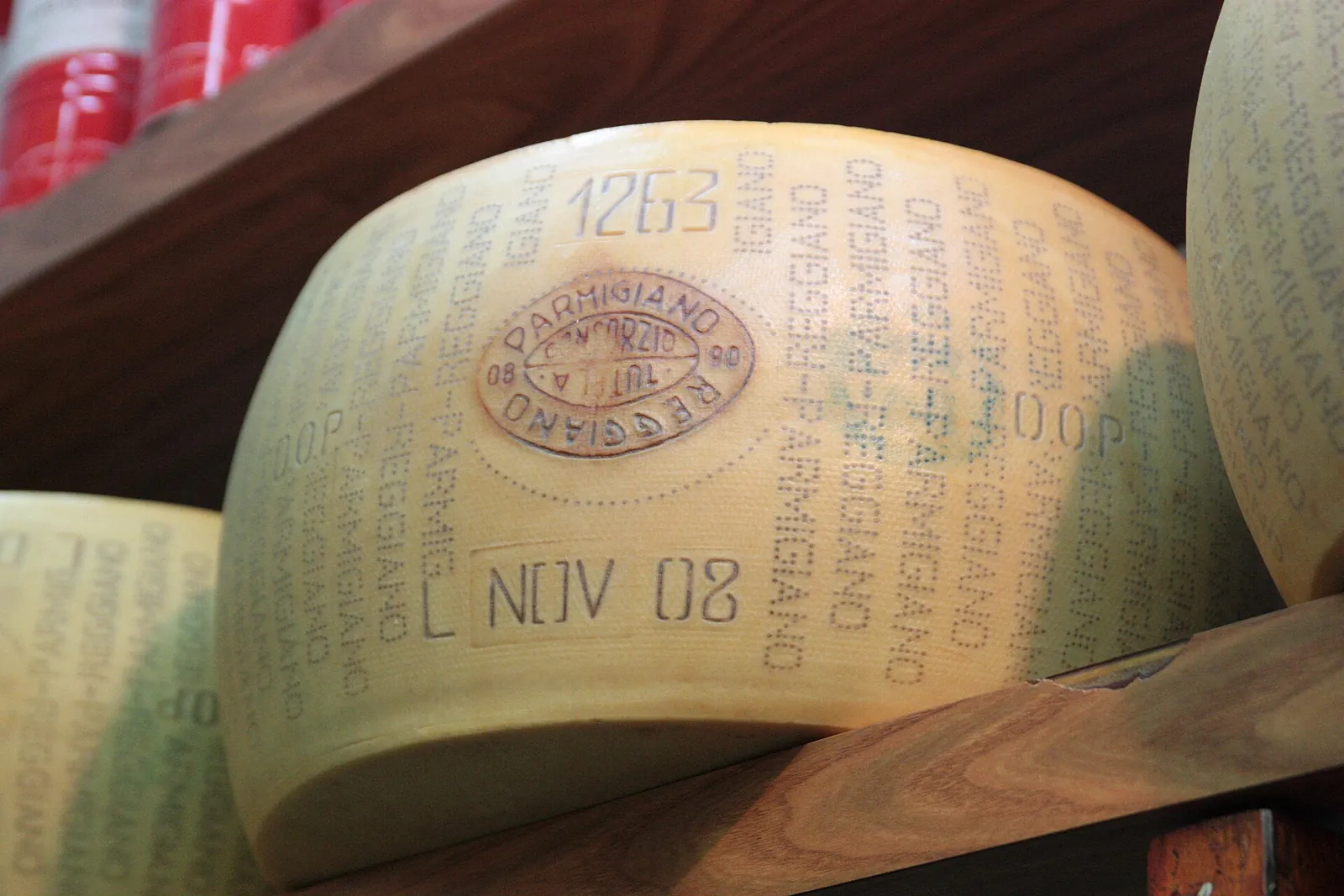 A Parmigiano-Reggiano wheel on a shelf showing its dotted rind lettering, a round seal and a production date stamp