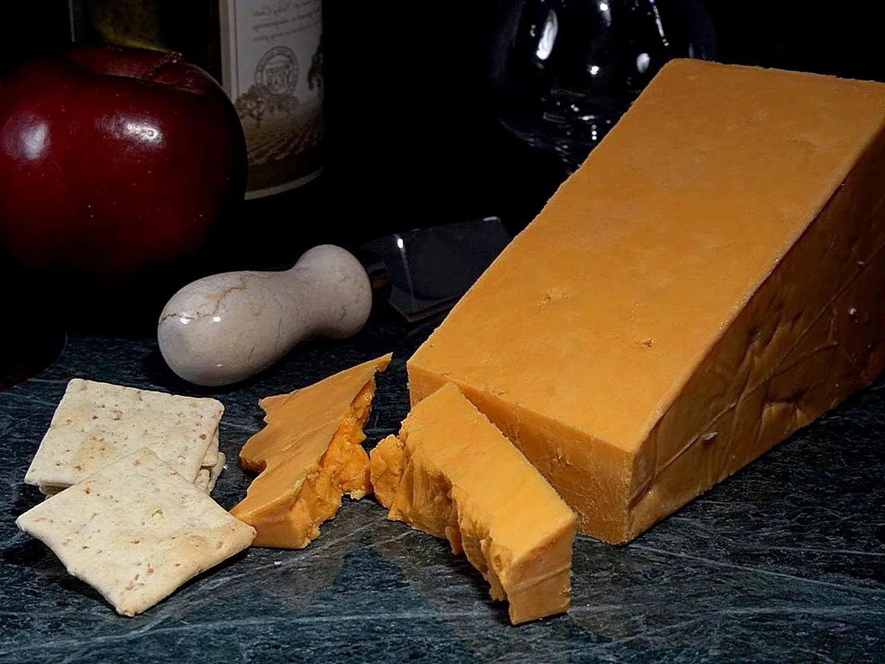 A wedge of deep orange Red Leicester with crackers and an apple