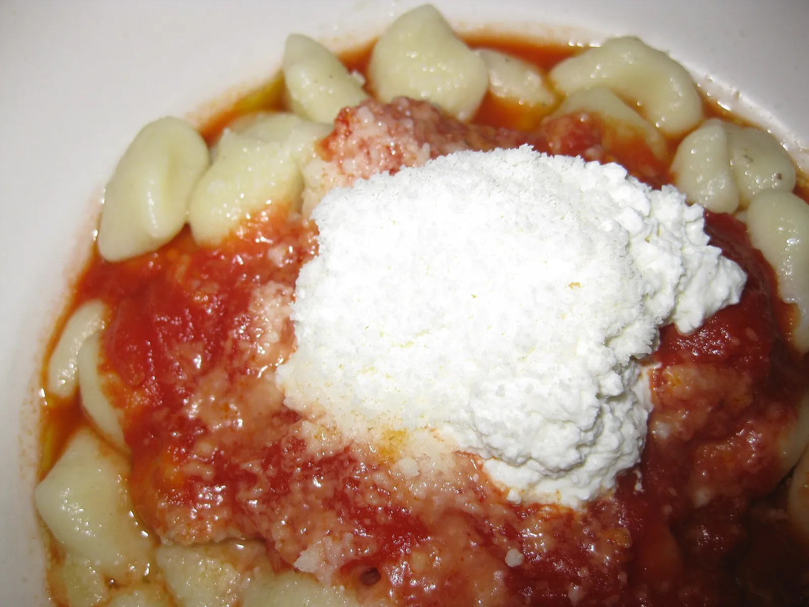 Small ricotta gnocchi in a bright tomato sauce, with a mound of fresh white ricotta and grated cheese spooned on top.