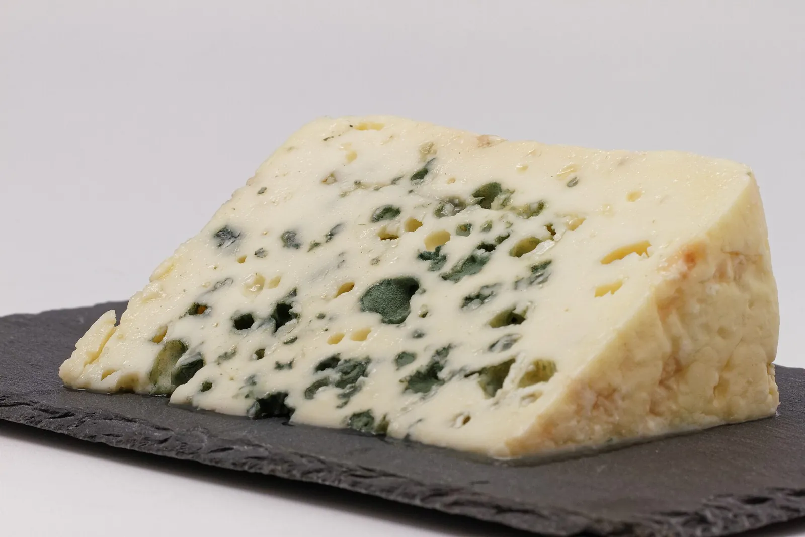 A wedge of Roquefort with blue-green veins through its white paste, on a slate board