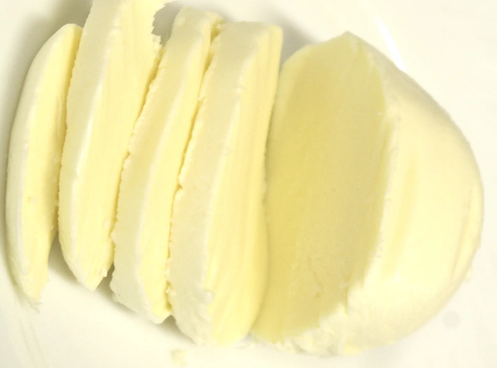 Several even slices of fresh white mozzarella fanned out on a white surface, with the cut faces smooth and moist.