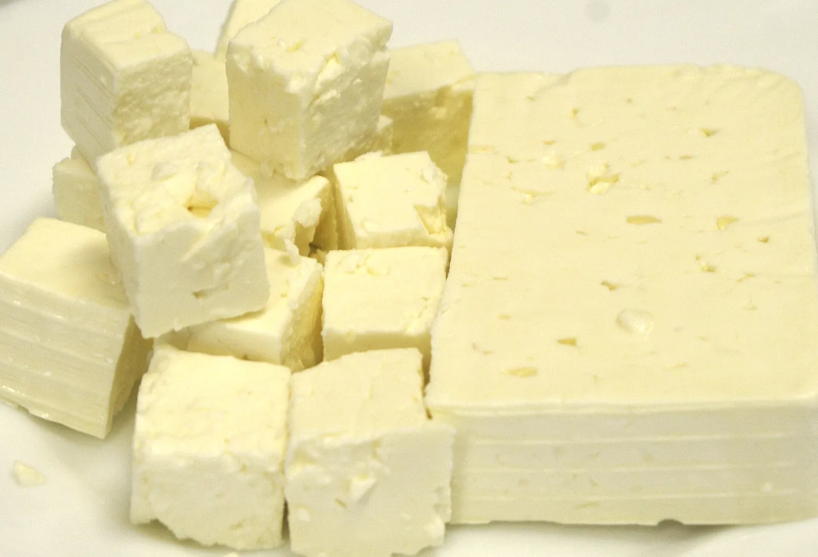 Fresh white feta cheese cut into cubes beside a larger slab, showing its small irregular holes and crumbly texture