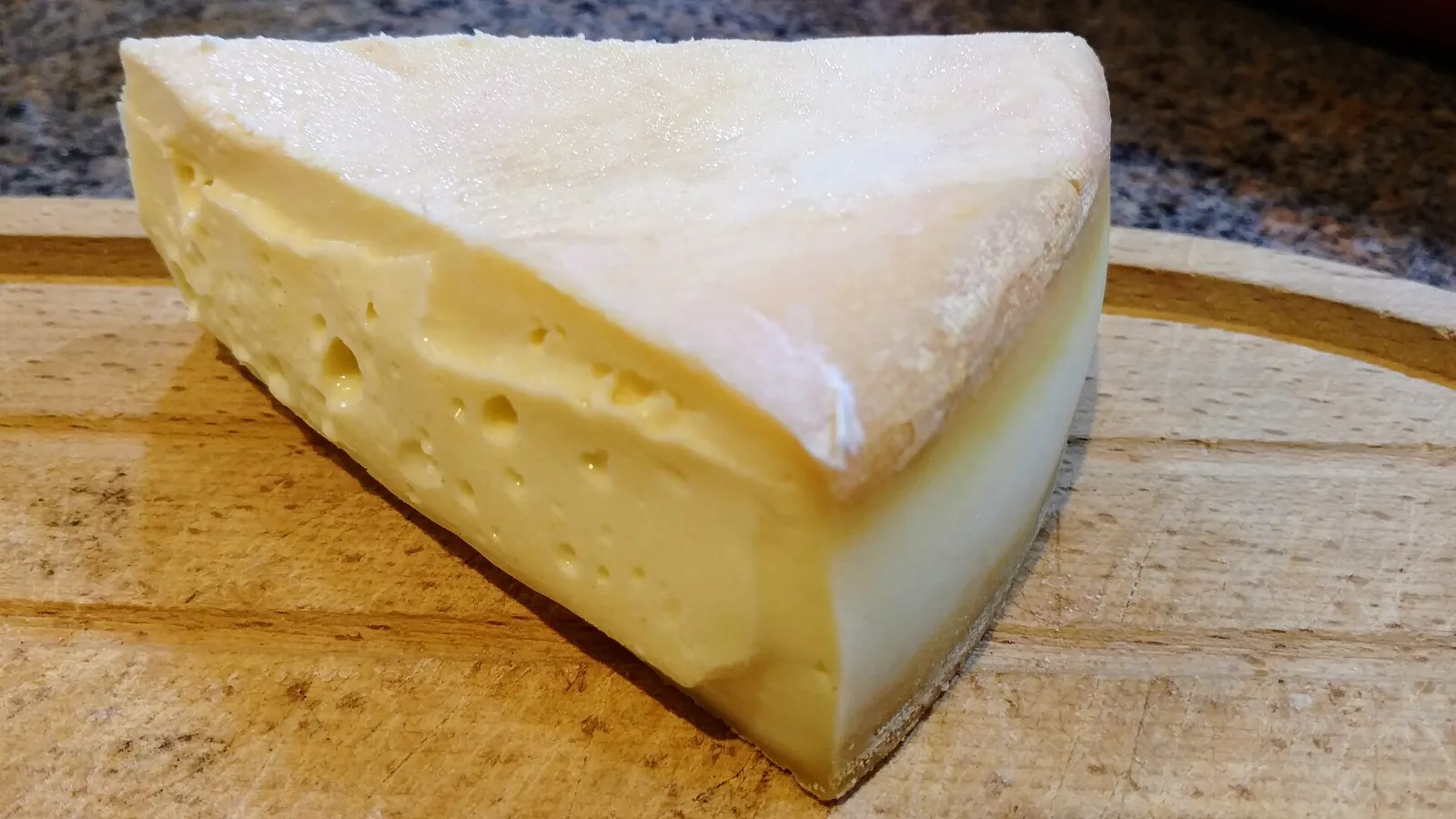 A wedge of Stinking Bishop with a pale sticky rind and smooth paste, on a wooden board