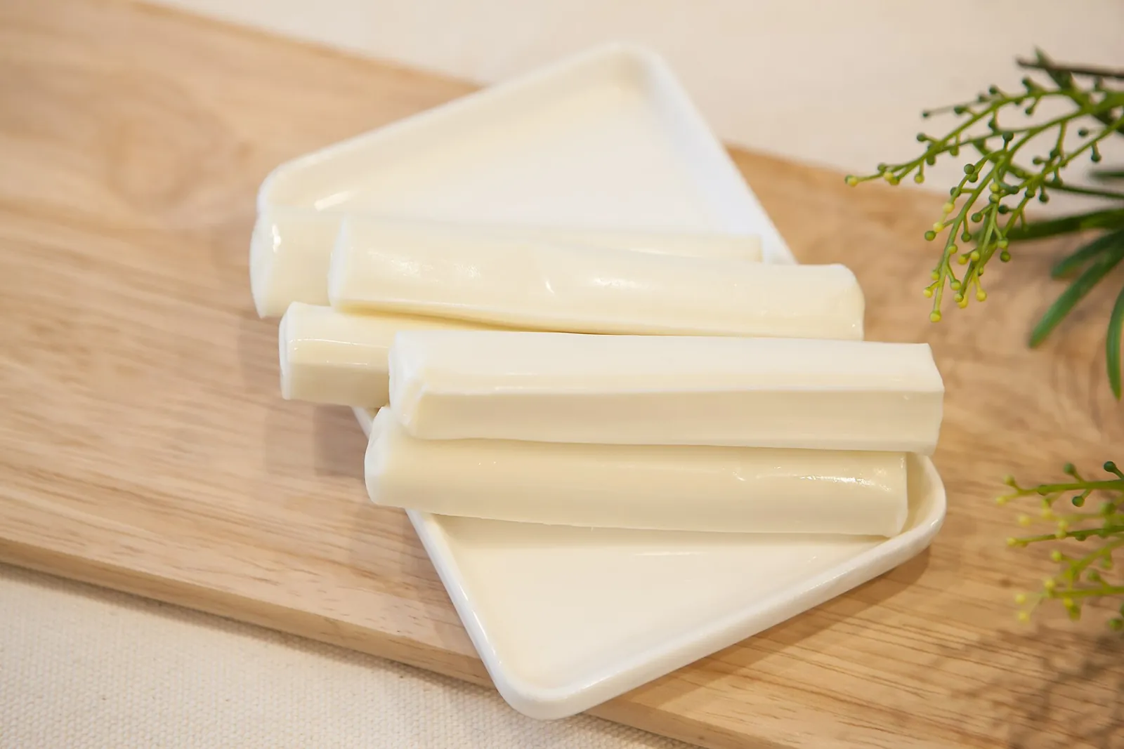 Sticks of string cheese on a white tray on a wooden board