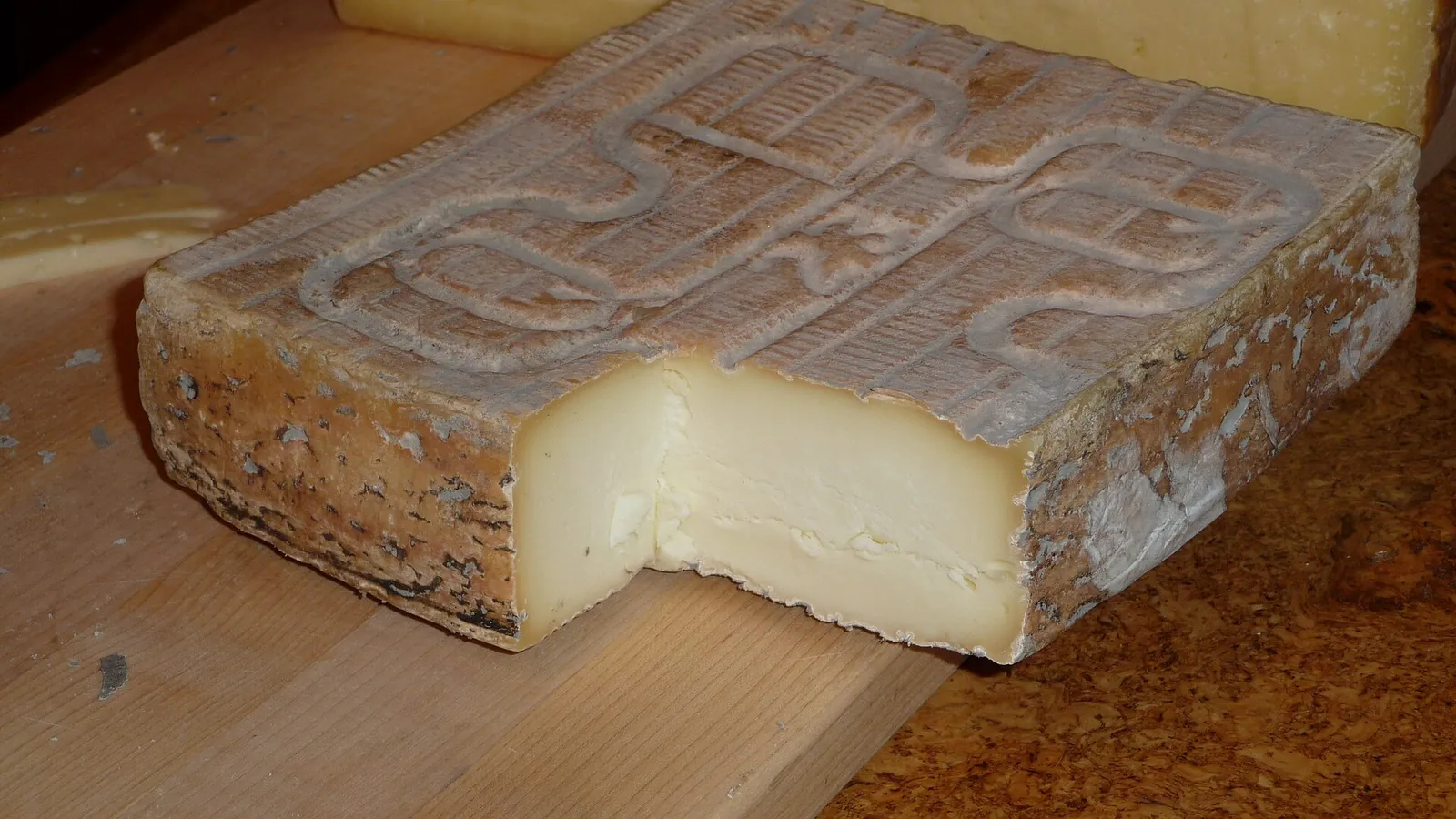 A square of Taleggio with a ridged pinkish rind, cut open to show the soft pale paste