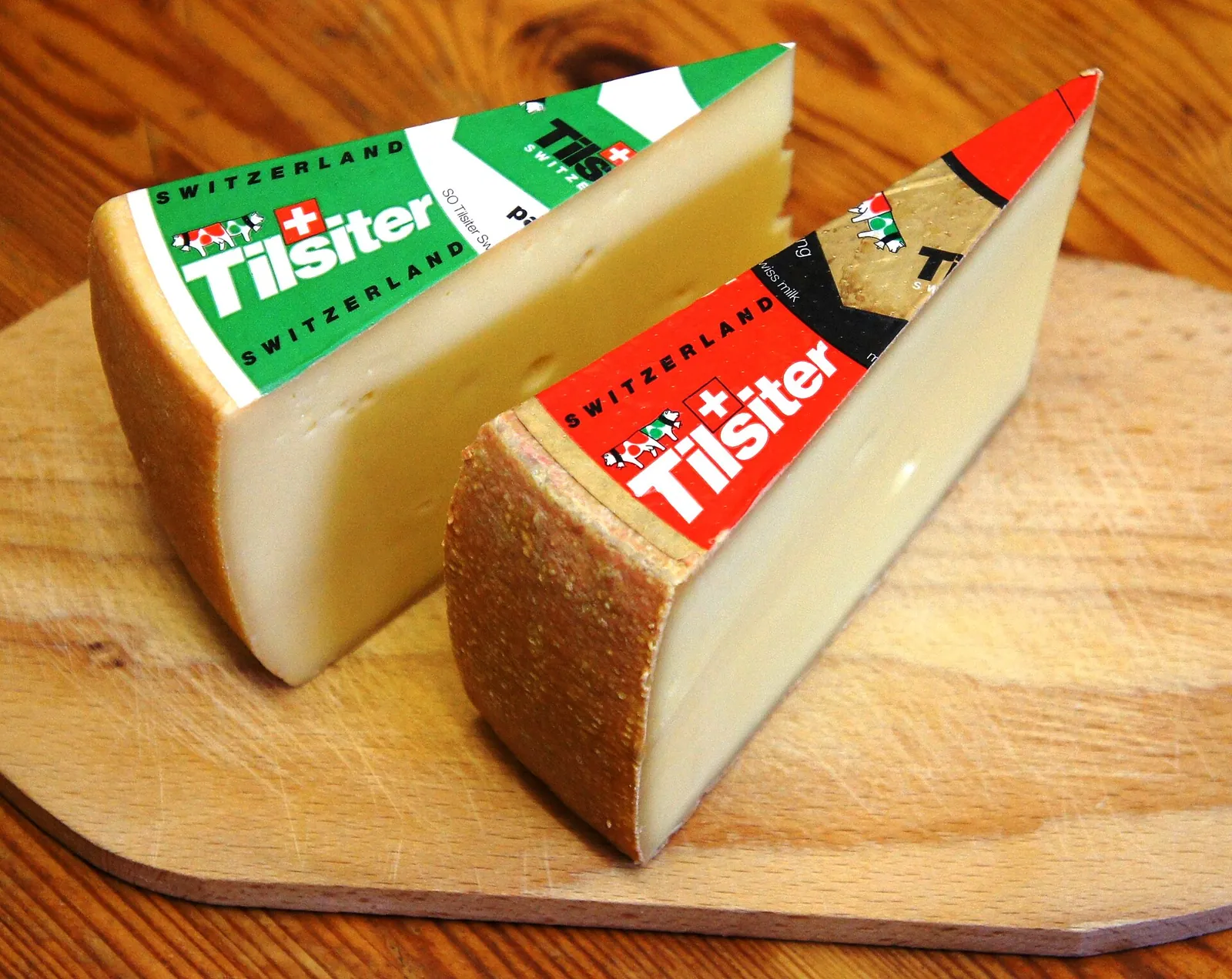 Two wedges of Swiss Tilsiter cheese with green and red paper labels on a wooden board