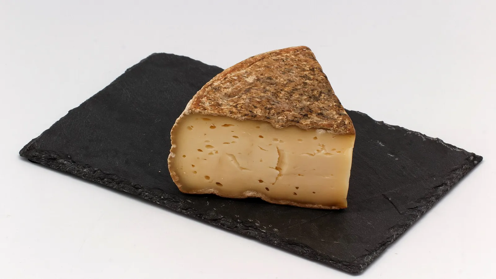 A wedge of Tomme de Savoie with a thick gray-brown rind on slate