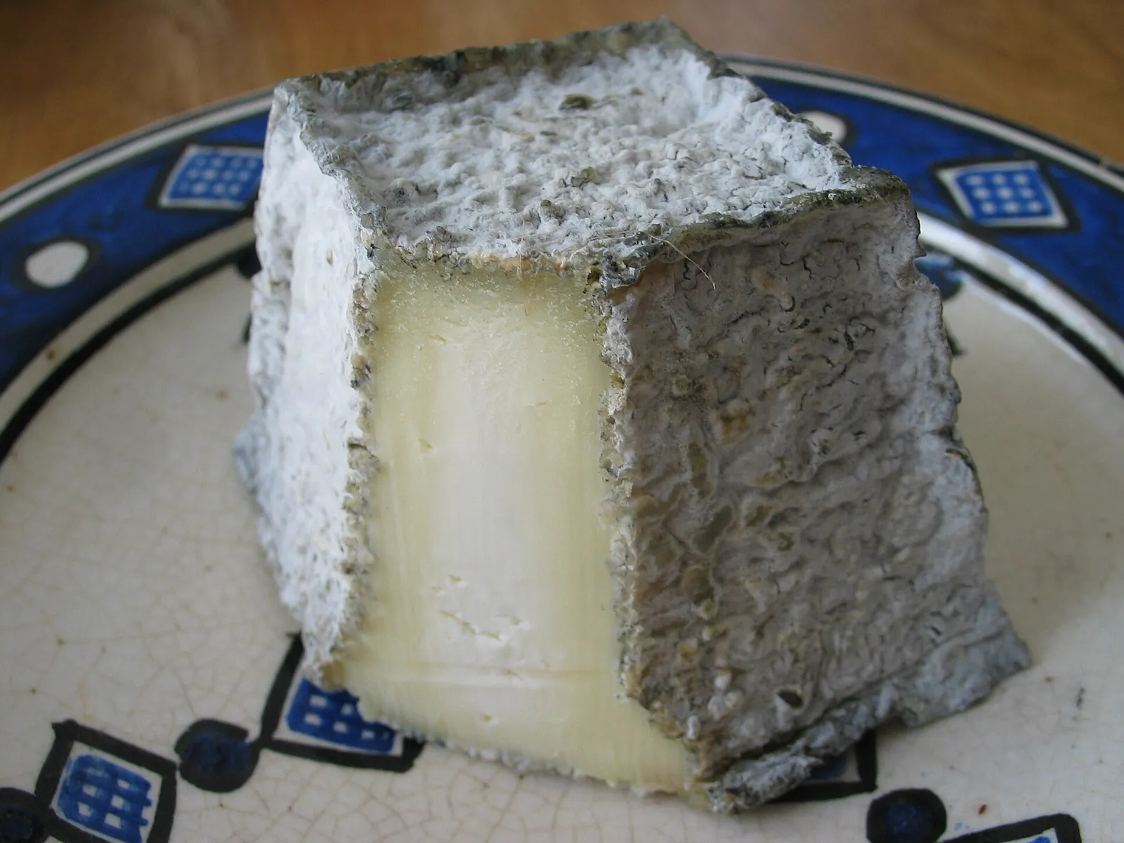A Valencay goat cheese pyramid cut open to show white paste beneath the ash dusted rind, on a patterned plate