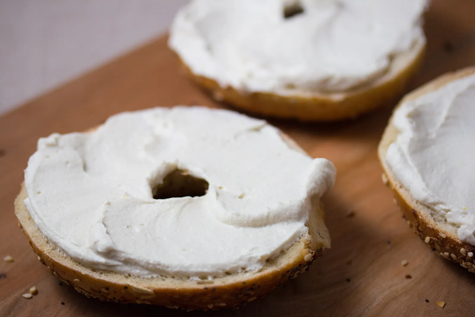 Sesame bagel halves spread thickly with creamy white vegan cashew cheese on a wooden board.